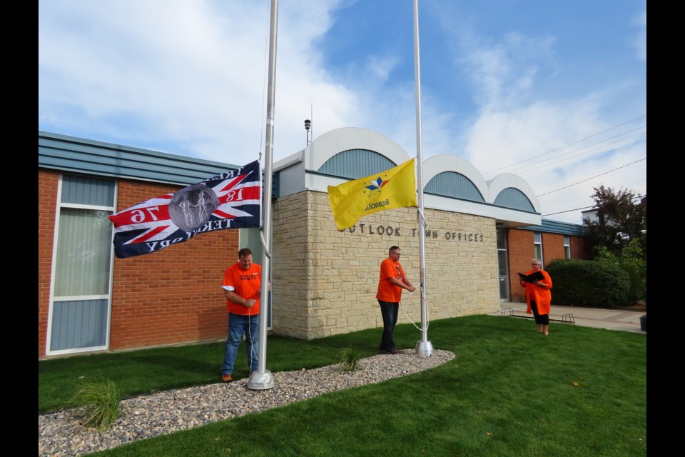 As Mayor Maureen Weiterman speaks, Kevin Trew and Justin Turton begin to raise the two flags above Outlook's town hall.