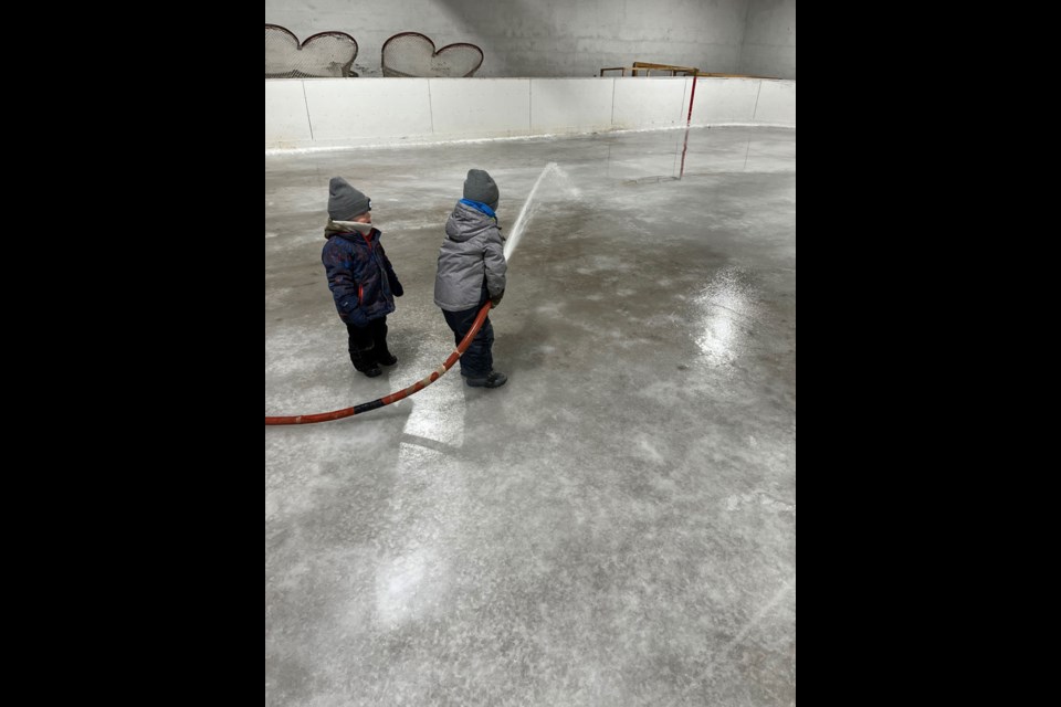A couple of little kids take a turn making ice, which they will skate on throughout the winter.