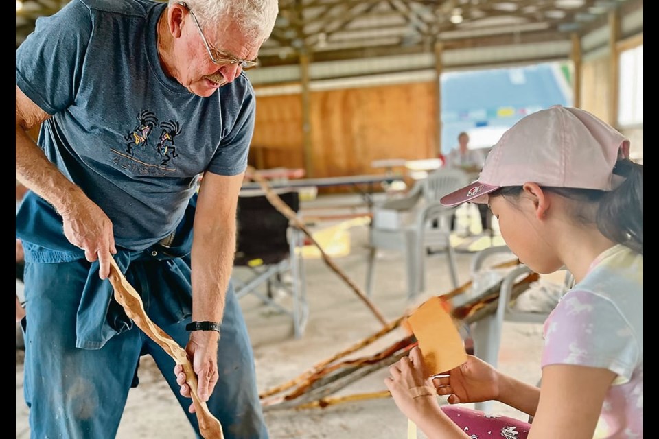 Journey Froese sands her walking stick using sand paper as Greg Mallett shows her how smooth the branch needs to be during a recent workshop. 