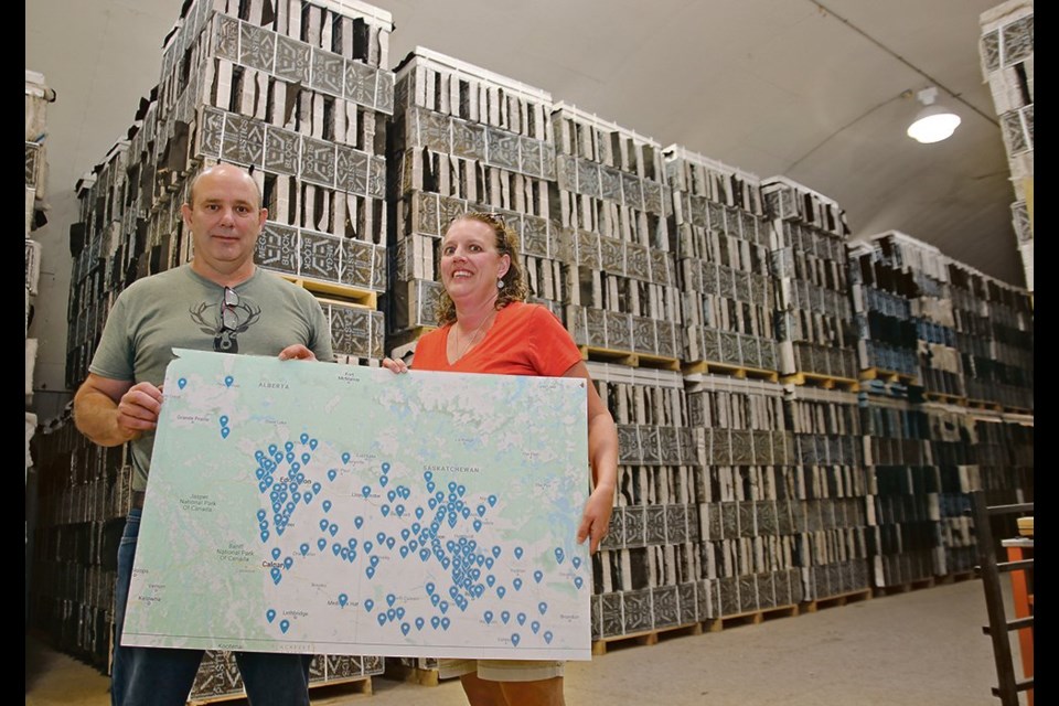 The Williams have sold their alfalfa seed across Western Canada as shown on the map they are holding, while the leafcutter bee larvae stacked in the nesting blocks behind them are sold across North America.