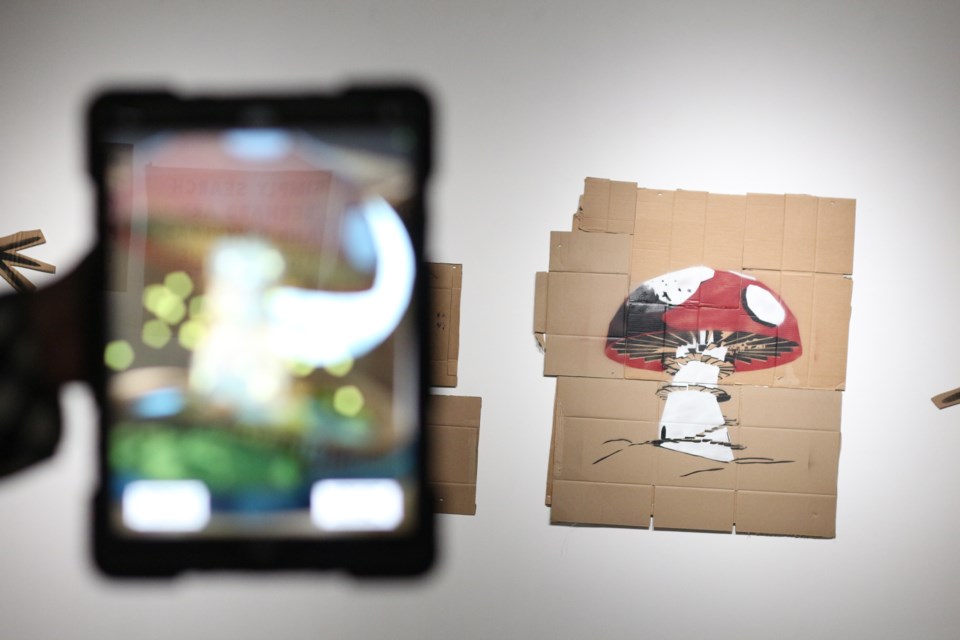 A spray painted stenciled mushroom on cardboard triggers the digital aspect of the art.