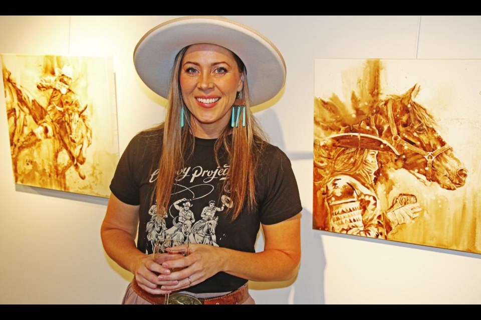 Artist Lauren Daae is shown with two of her coffee-painted works, with the one at right one of her personal favourites from this exhibition, showing now at the Weyburn Art Gallery.