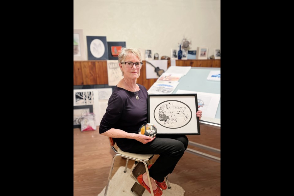 Unity artist, Faye McCubbing, poses with some of her artwork - a painting and a creatively painted rock that resembles a prairie rabbit.