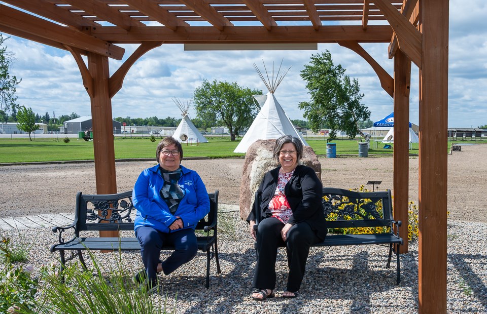 Diane Pooyak and Shirley Maze sit in the pergola area in front of where the Tipi Village is located.