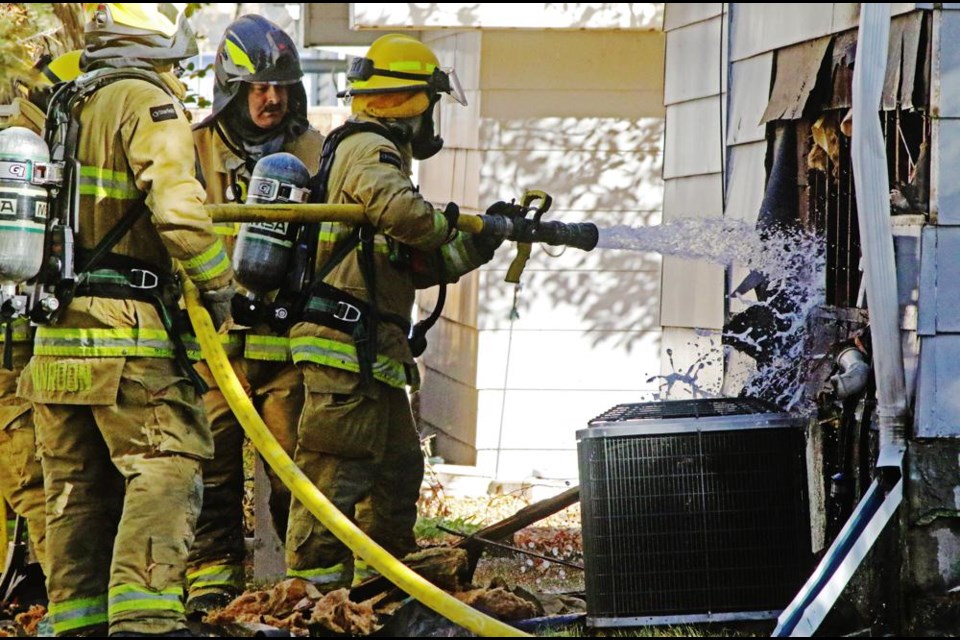 A Weyburn fire fighter fires water into a hole in the side of a house on 10th Street and East Avenue, where there was a fire on Saturday afternoon.