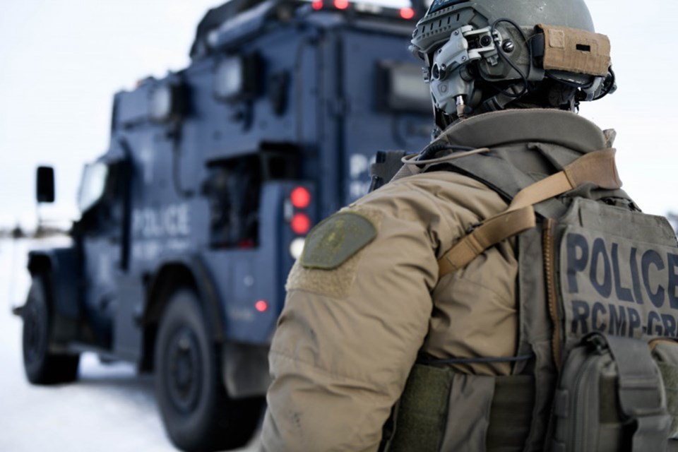 An armed RCMP officer stands near a tactical vehicle.