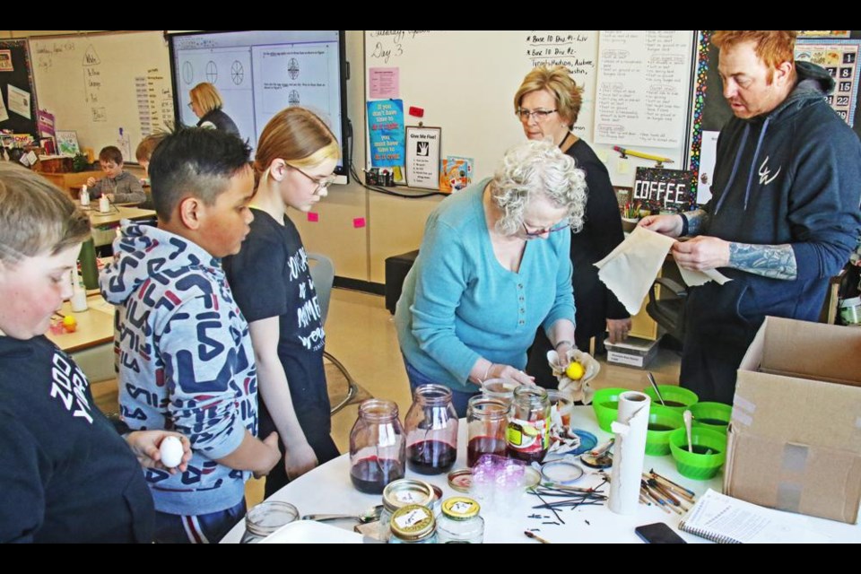 Grade 5 students lined up to get their eggs dyed yellow, with Bonnie Lillejord and Tyler Hillstead helping out at right.