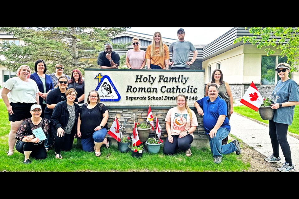 The central office staff for the Holy Family Roman Catholic Separate School Division gathered after making planters which were donated to the Southeast Newcomers Services, to give to new residents of Weyburn. Above the sign are Father Val Amobi, Wendy Hockley, Brooklyn Lund and Kyle Hambly. Left of the sign are Amy Scott-Wawro, Claire Fingler, Laurieanne Bendtsen, Terry Jordens and Maureen Daoust. In front are Lynn Colquhoun, Kari Erb, Becky Tuchscherer, Jasmine Lund and Michael Kaip, while at right are Maria Barranco, SWIS worker, and education director Gwen Keith.