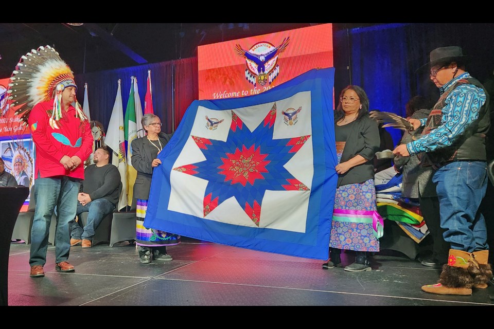 Saskatoon Tribal Council Chief Mark Arcand, left, looks on as Chiefs Ava Bear (Muskoday First Nation), second left, and Tricia Sutherland (One Arrow  First Nation) present a blanket.