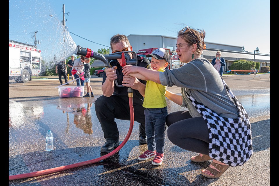 A child gets help from a firefighter and his mom so he can try out the fire hose during a celebration of community spirit in Battleford Friday. Battleford's volunteer fire department was a big part of the event, and the firehose was a big hit with the kids.