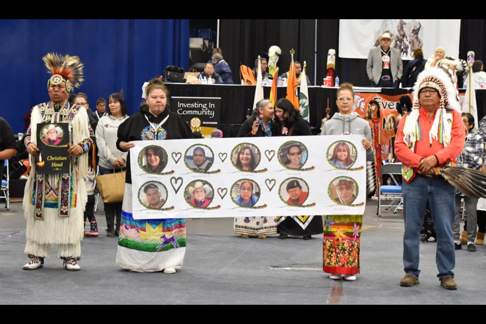 Two relatives of the Sept. 4 stabbing victims hold a banner that bears the photos of their loved ones as they were joined by Chakastaypasin Band Chief Calvin Sanderson, right.