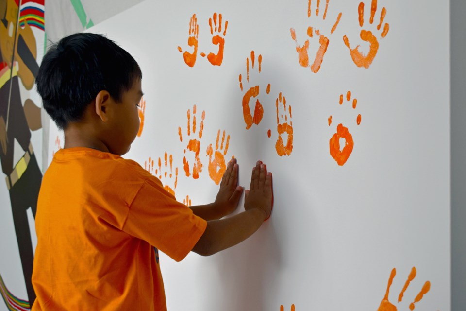 A student from École Victoria leaves his handprints on a canvass to memorialize residential school victims on Monday, Sept. 26, at the Métis Nation-Saskatchewan office downtown.