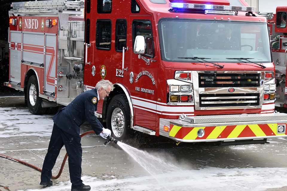 Firefighter Rob Beatch sprays water from the old Engine-22 onto the new Engine-22 to 'baptize' the new truck as it joins the fleet.