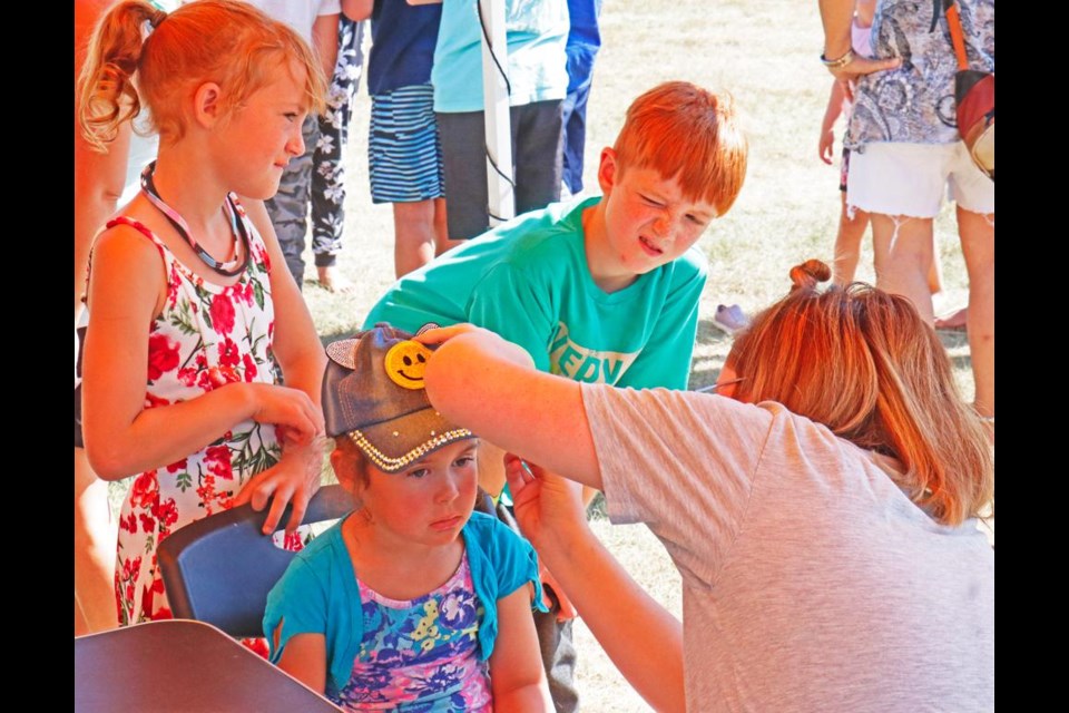 A sister and brother wait their turn as their youngest sister gets her face painted