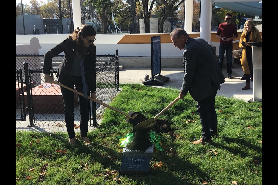 Mayor Sandra Masters and Minister Don McMorris pour the sod over the time capsule placed at Wascana Pool, marking the end of the first year of the renewed facility.