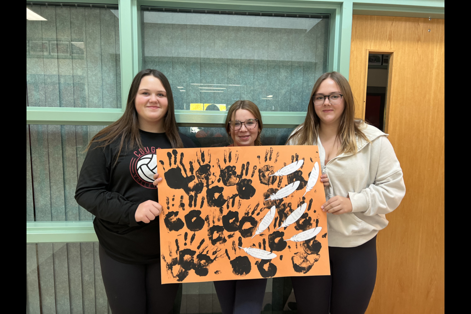 Grade 8 students, from left: Heidi Parmley, Kaelyn Shukin and Natalie Kosar created a poster featuring quotes on truth and reconciliation, and included black handprints to emphasize that every child matters. 

