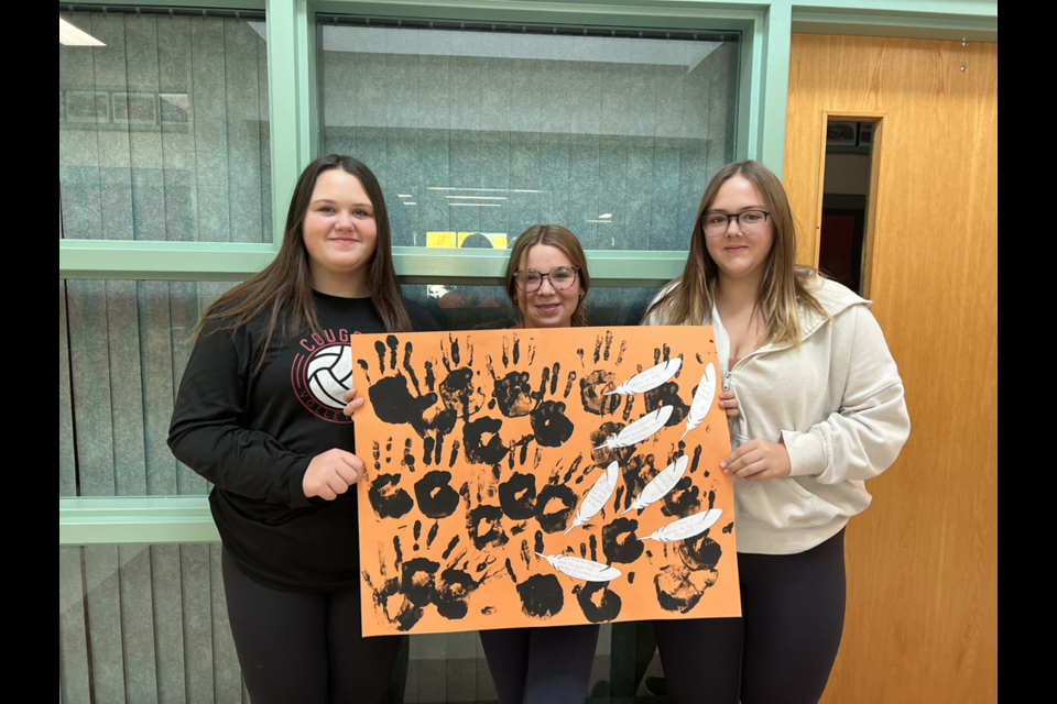 Grade 8 students, from left: Heidi Parmley, Kaelyn Shukin and Natalie Kosar created a poster featuring quotes on truth and reconciliation, and included black handprints to emphasize that every child matters. 

