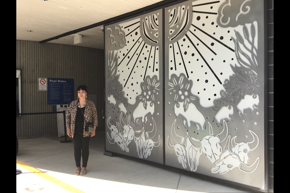 Larissa Kitchemonia stands next to her design at the front gate of Wascana Pool.