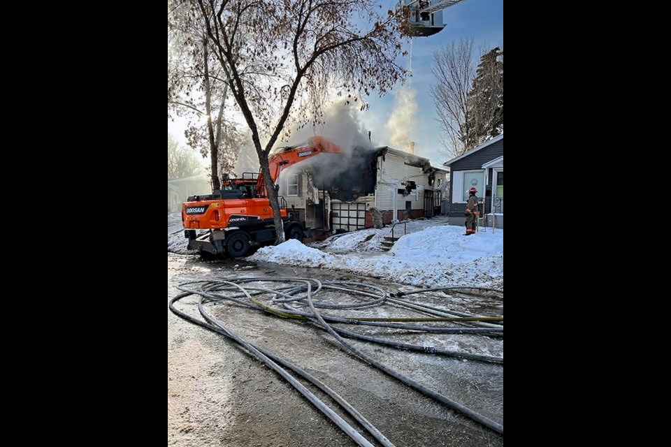 A backhoe pulls apart portions of the structure to help firefighters extinguish the fire.