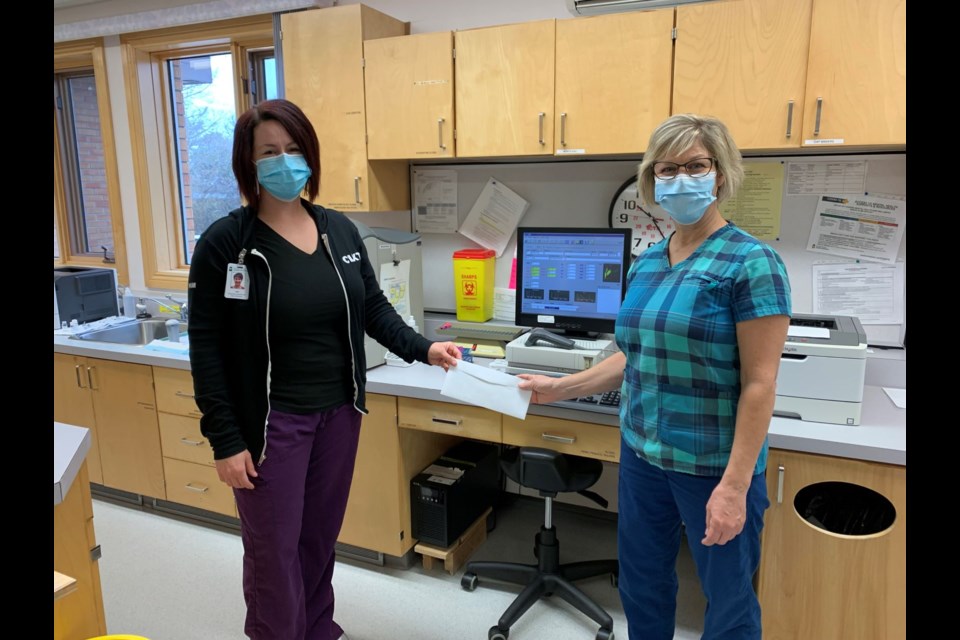 Palliative Care secretary-treasurer Marla Schlenker presenting a $4,500 donation to Kim Penney, who are standing in front of the CBC Blood Testing Machine that is soon to be replaced. 