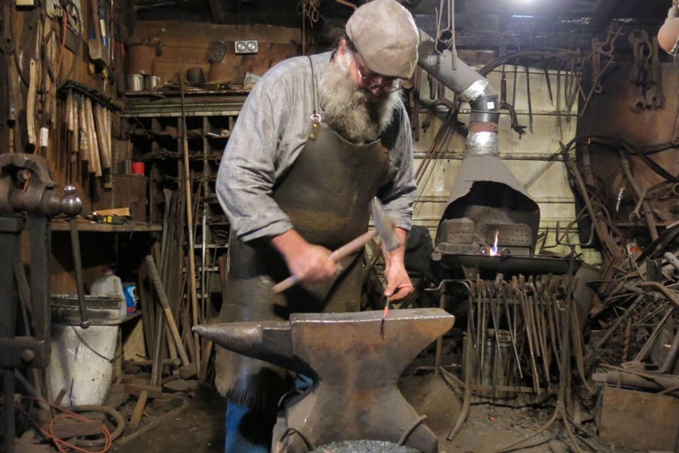 Working out of his workshop, Jim hammers at a piece of hot metal against the anvil.