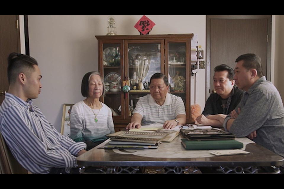 The Chow family and director Weiye Su seated around a dining table covered in photo albums. 