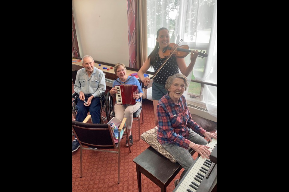 Clara Olson on the piano at Rose Gill Lodge, along with violinist granddaughter Quinn Baynham and daughter Hilda Eberle of the Battlefords. Spoon player Henry Konopelski, another senior, decided to join them for a fun hour of oldie goldies.