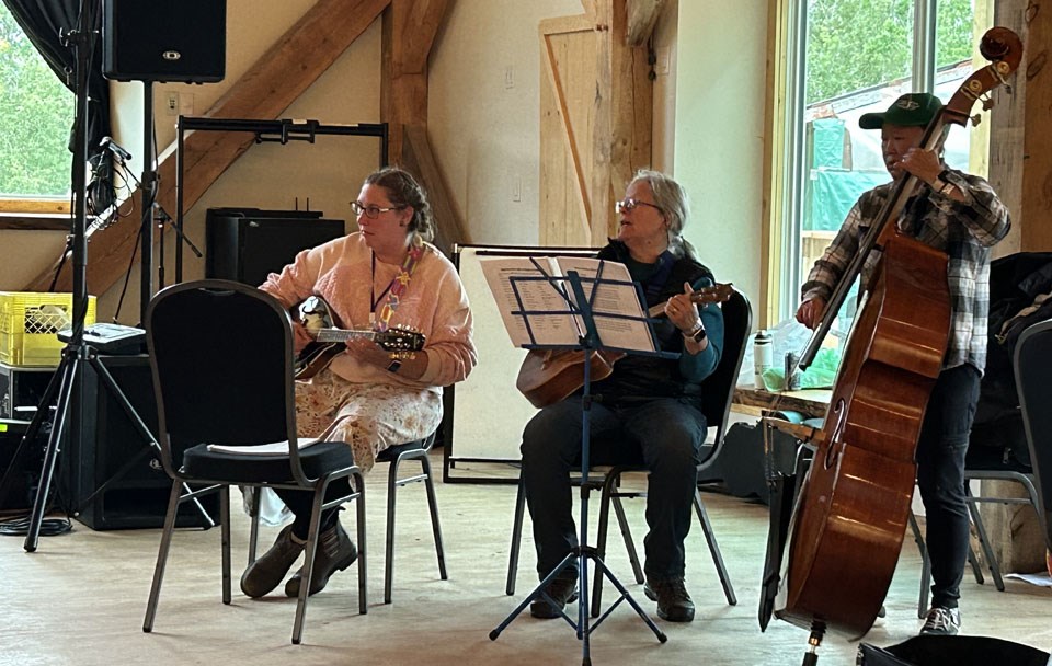 Three out of 12 with different instruments doing back up music for the “ sing song circle” in Jack Milligan Hall, Ness Creek late Saturday afternoon, while performances were still going on the outside large stage — Carmen Bellhumeur (home unknown), Suzanne Baril and May Mah-Paulson from Victoria, Vancouver Island. 