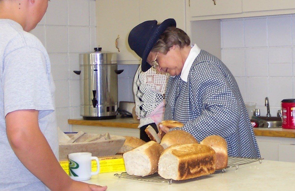 A volunteer dressed in period clothing, slices bread for an eager and hungry young man at the grand opening.