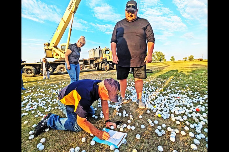 Garnet Hart of the Weyburn Rotary Club fished the winning balls out of the hole, recording the number of each to determine the top three cash prize winners. Watching above him is Jeff Ward of the Estevan club, and in. behind is Estevan club president Terry Williams.