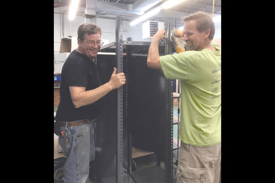 Veteran members Cam Leslie and Phil Guebert share a laugh as they assemble shelving at Equinox Theatre’s new storage area in the back of Outlook Printers.