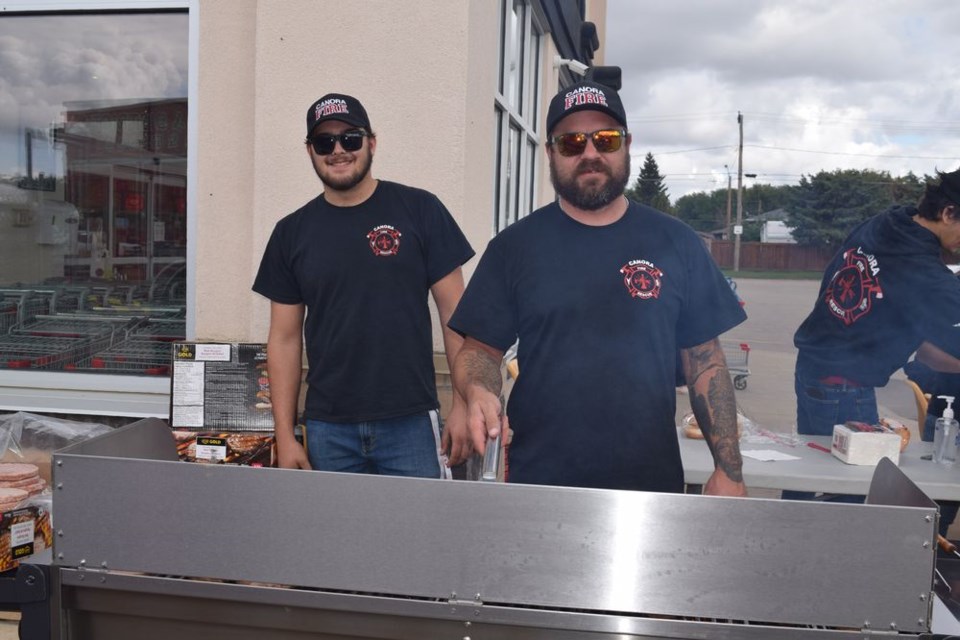 Assisted by firefighter Alden Baron, left, fire chief Devon Sawka performed the important task of flipping burgers, while the rest of the firefighters and their families were busy looking after the burger orders.