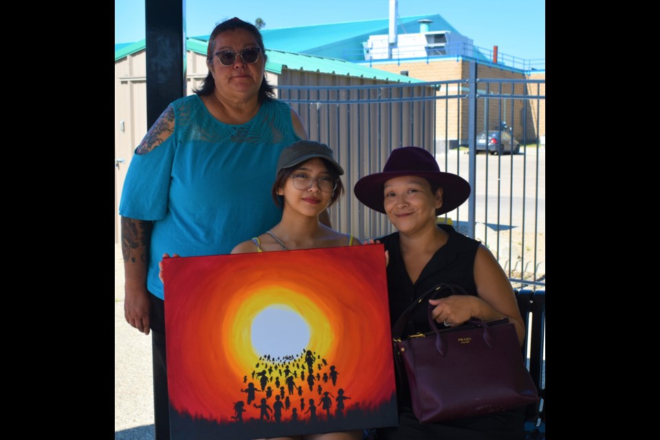 Kylie Severight, seated left, poses with her painting together with her mom Heather, seated right, and grandmother Marlene Lumberjack.