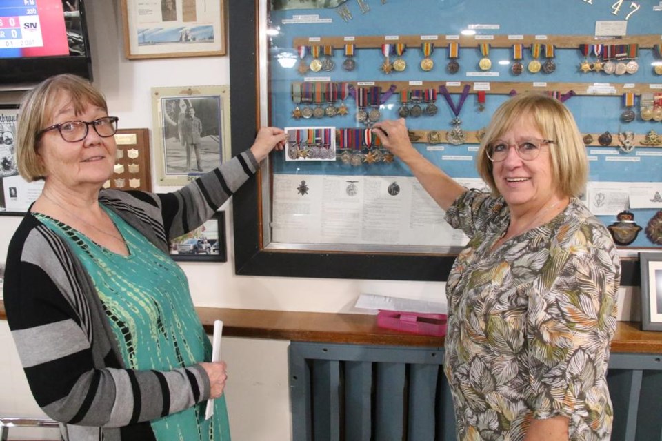 Janice Howden, left, and her cousin Sharon Clarke held up war medals along with a set on display at the Weyburn Legion. Janice has medals from Don, whose medals included the Distinguished Flying Medal; the medals in the case were for Rex, who died on a bombing run during the Second World War; and Sharon is holding Jim’s medals. All seven of the boys of their grandparents, T.H. and Eva Mitchell, enlisted in the war, and only Rex did not come home. (Updated to indicate Howden and Clarke are cousins, not sisters.)