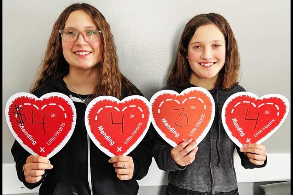 Myla and Morgyn Moule hold up hearts to show the total dollars raised by their cookie sale for the Mending Little Hearts Fund in February