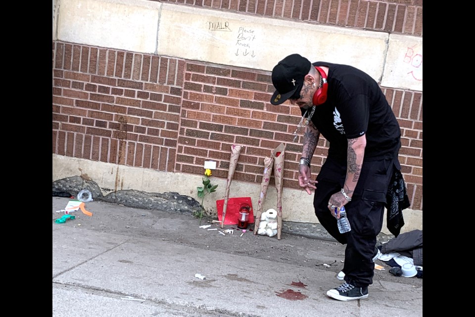 An unidentified man kisses his hand then places it on the blood stain on the side walk Tuesday morning in Saskatoon on 20th Street.