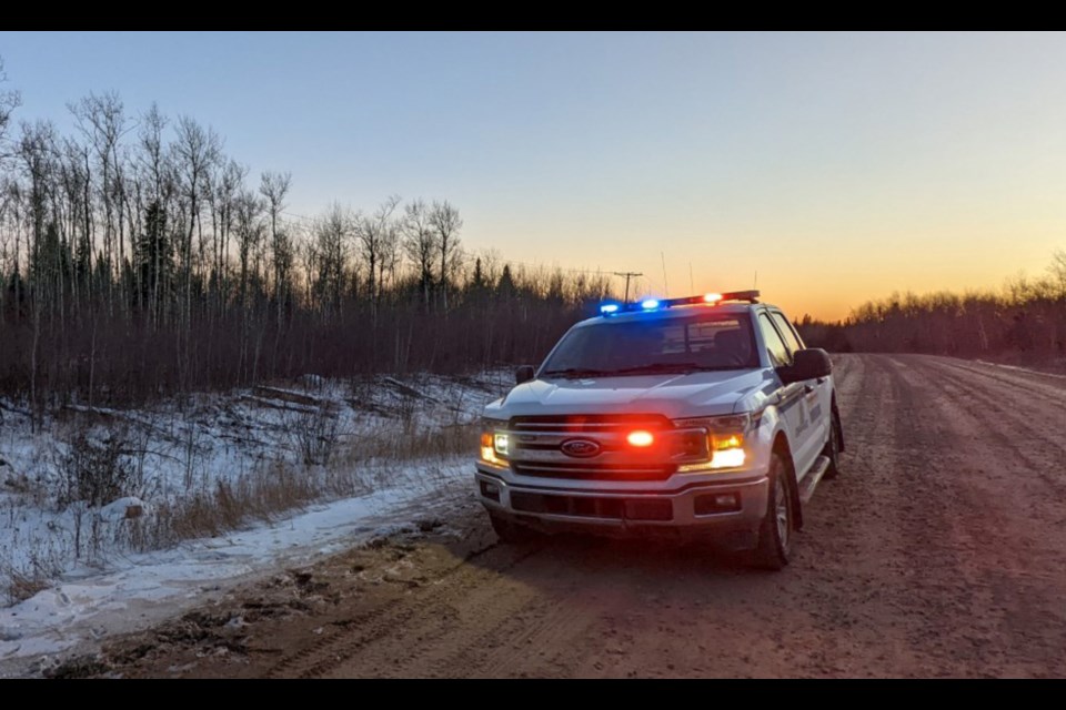 An RCMP vehicle sits at the roadside near the dense bush.