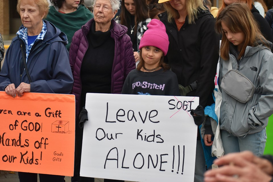 A young protester meets the gaze of the camera as she holds a sign that says, "leave our kids alone."