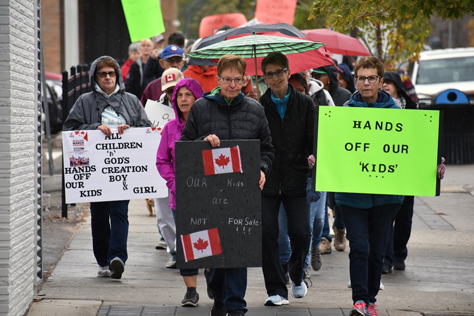 The march moves down 101st Street, with signs that tell people to keep their hands off children, and that children aren't for sale.