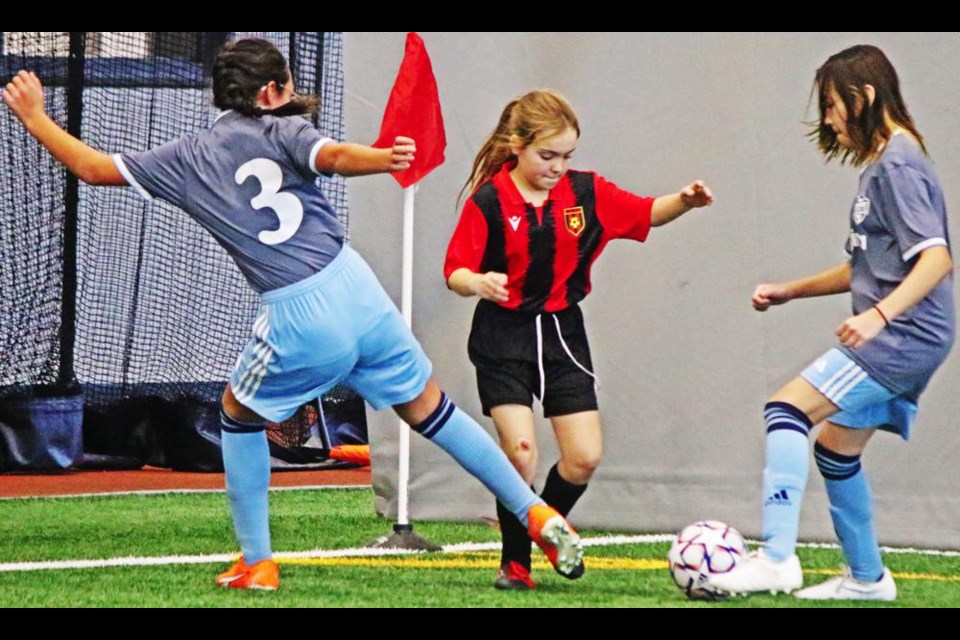 A Weyburn U11 player tried to get the ball out of the corner with two FC Regina players going against her.