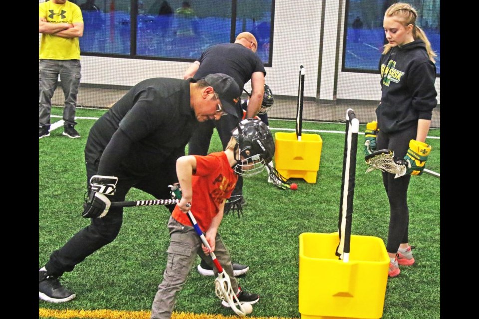 A young boy tries out lacrosse, here learning how to scoop up the ball with the racket.