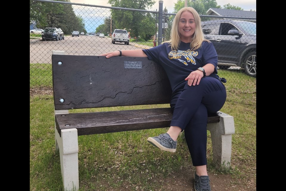 Unity ball mom and minor ball volunteer, Roxanne Greenwald, sits proudly on the newly erected bench in memory of long-time ball supporter Oscar Housen.