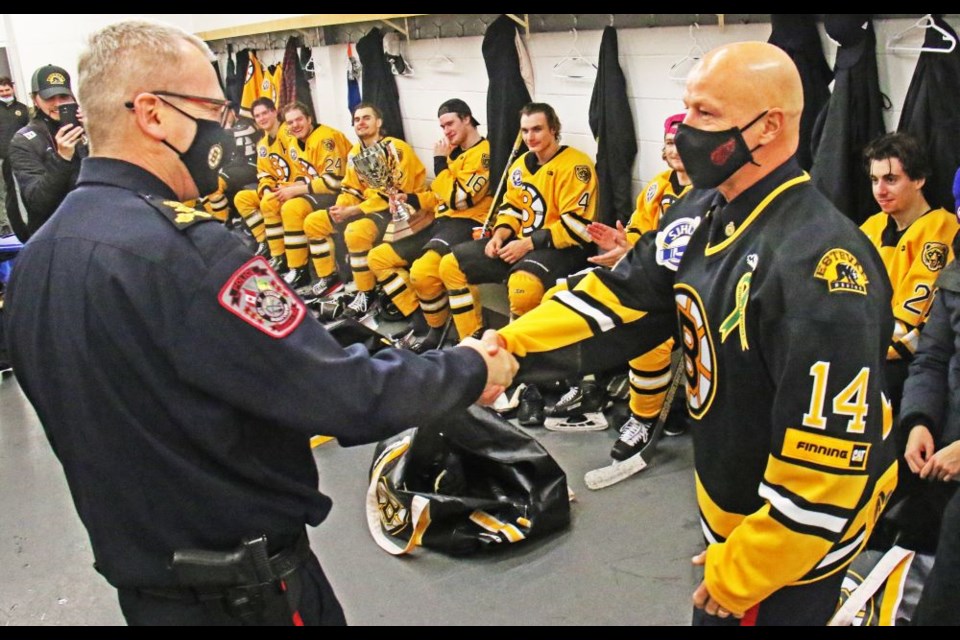 Weyburn Police Chief Jamie Blunden, wearing an Estevan Bruins jersey, congratulates Estevan Police Chief Richard Lowen on the Highway 39 Cup victory while members of the Bruins look on. 