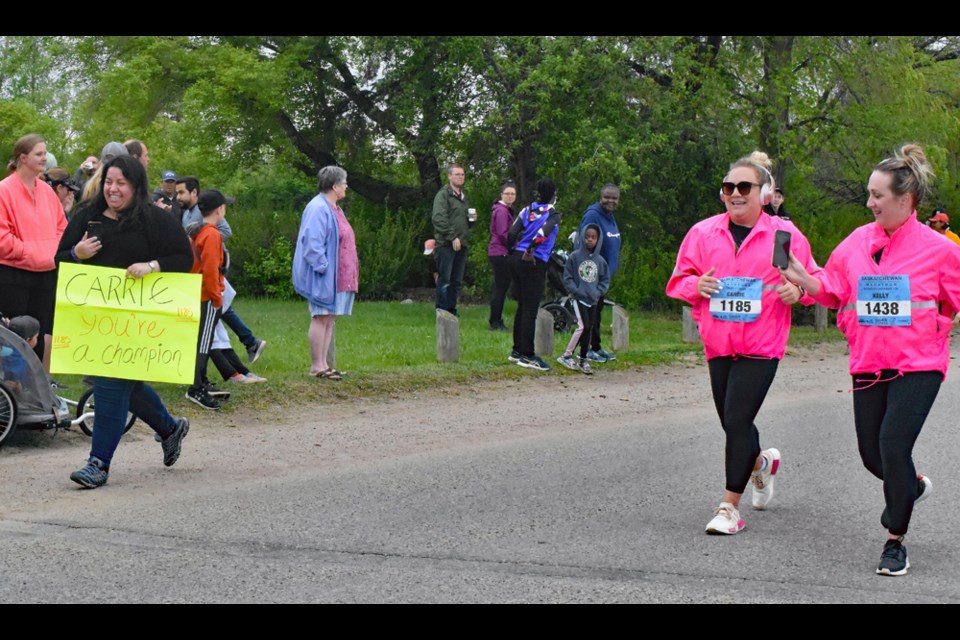 Carrie Gauthier of Saskatoon, centre, is cheered on by one of their friends, left, as she and Kell Schira near the finish line in the 10-k race of Sunday's Saskatchewan Marathon.  