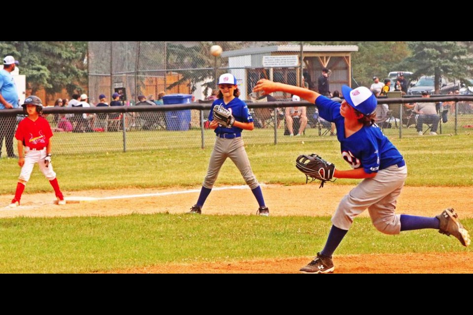 Pitcher Kaleb Thiessen throws a pitch as a Saskatoon Cardinal runner watches from third base.