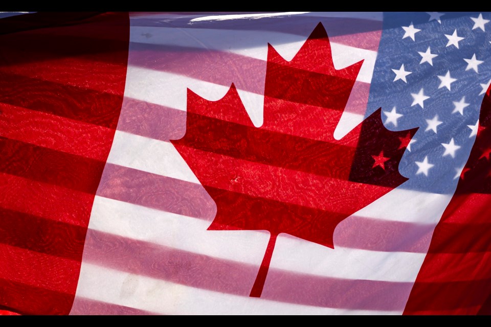 FILE - Sunlight shines through the flags of Canada and the United States, held together by a protester outside on Parliament Hill in Ottawa, Feb. 1, 2025.(Justin Tang/The Canadian Press via AP, File)