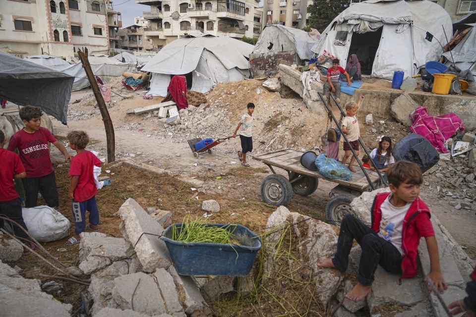 Palestinian youth and children are seen at a tent camp set up amid war-damaged infrastructure in Gaza City, Monday, June 23, 2025. (AP Photo/Jehad Alshrafi)