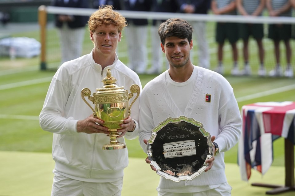 Italy's Jannik Sinner, left, celebrates with the trophy after beating Carlos Alcaraz of Spain, right, to win the men's singles final at the Wimbledon Tennis Championships in London, Sunday, July 13, 2025. (AP Photo/Kin Cheung)