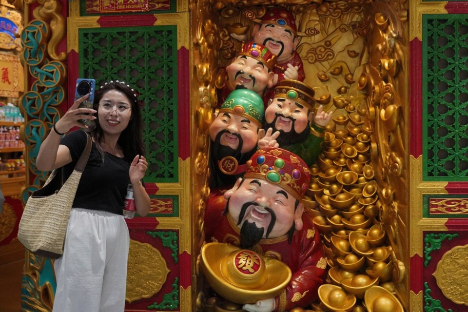 A woman takes a selfie with gods of fortune displayed outside a store selling prosperity items at a shopping mall, in Beijing, Monday, July 14, 2025. (AP Photo/Andy Wong)
