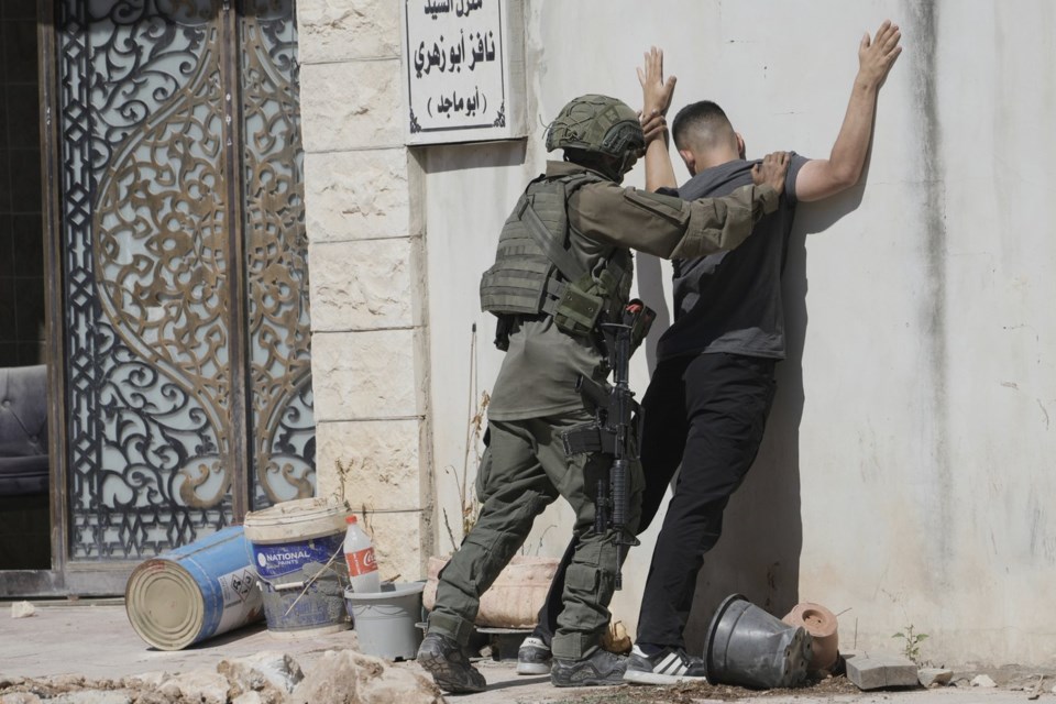 An Israeli soldier body search a Palestinian man in the West Bank urban refugee camp of Tulkarm residence evacuate their homes and carry their belongings as the Israeli military continues its operation in the area ahead of planned home demolitions by Israeli security forces, Sunday, July 6, 2025. THE CANADIAN PRESS/AP-Majdi Mohammad